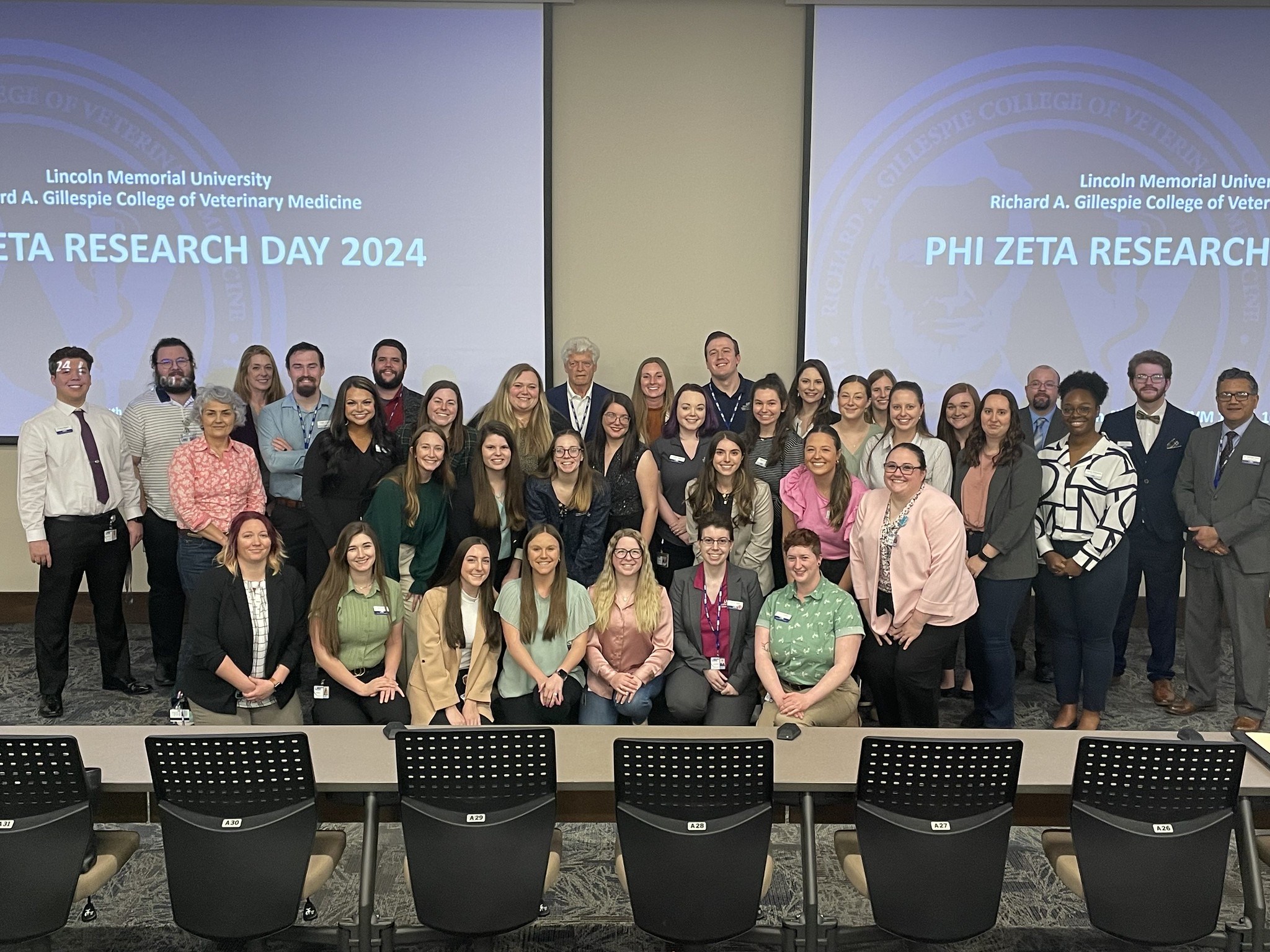 A large group of people smiling in front of a projector that says Research Day 2024